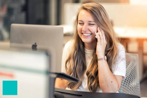 Een vrolijke vrouw praat aan de telefoon terwijl ze achter haar computer werkt.