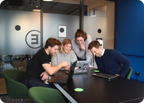 Een team van vier personen werkt samen op laptops en brainstormt over ideeën aan een moderne kantoortafel.