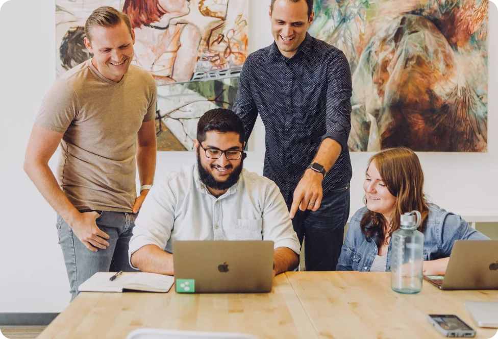 Een team van vier professionals die samenwerken op een laptop en ideeën brainstormen.