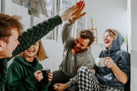 Vier vrienden geven elkaar een high five, lachend en genietend van een warm drankje.